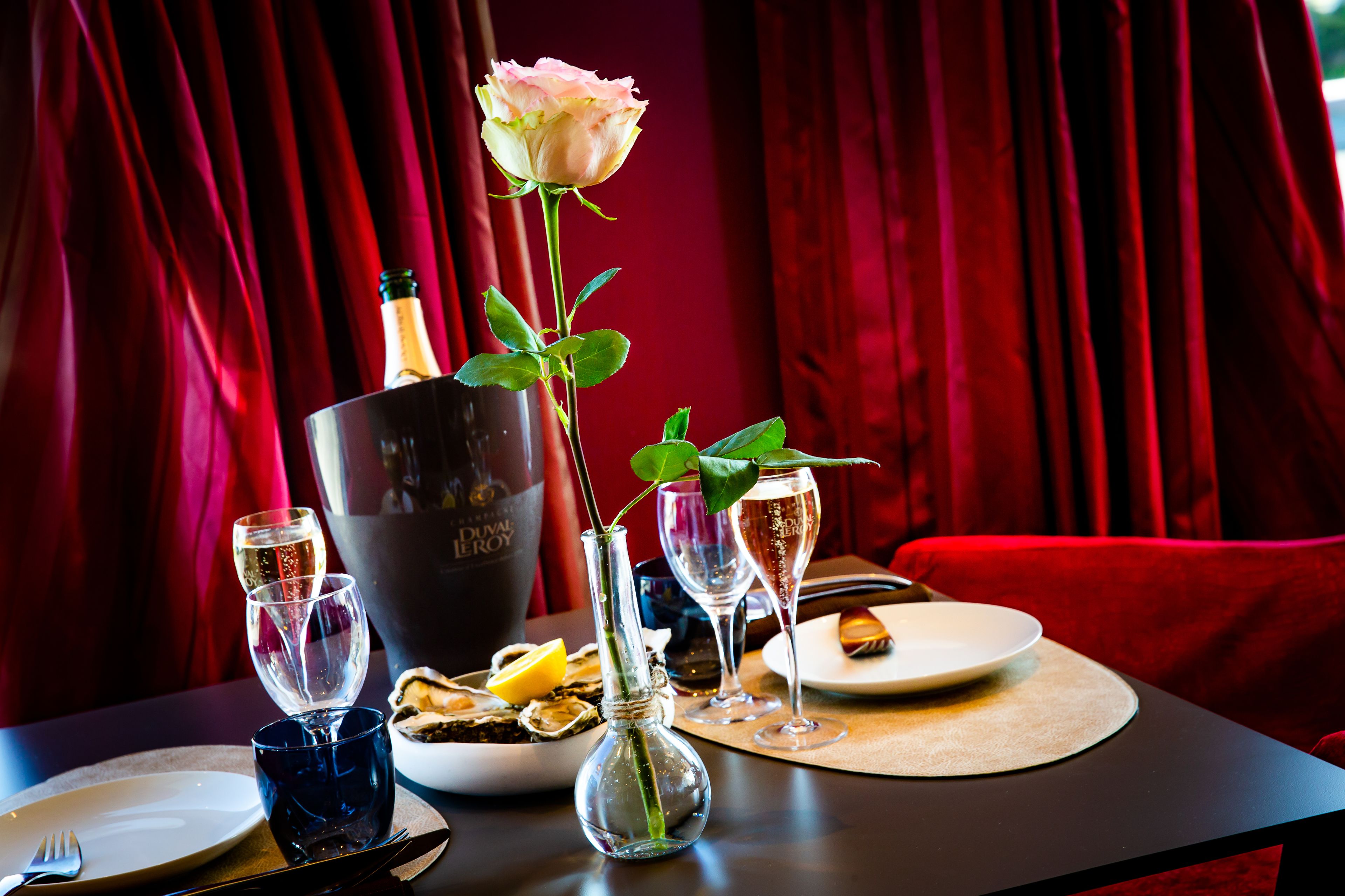 Una mesa de comedor con una rosa, copas de champán y una botella de vino.