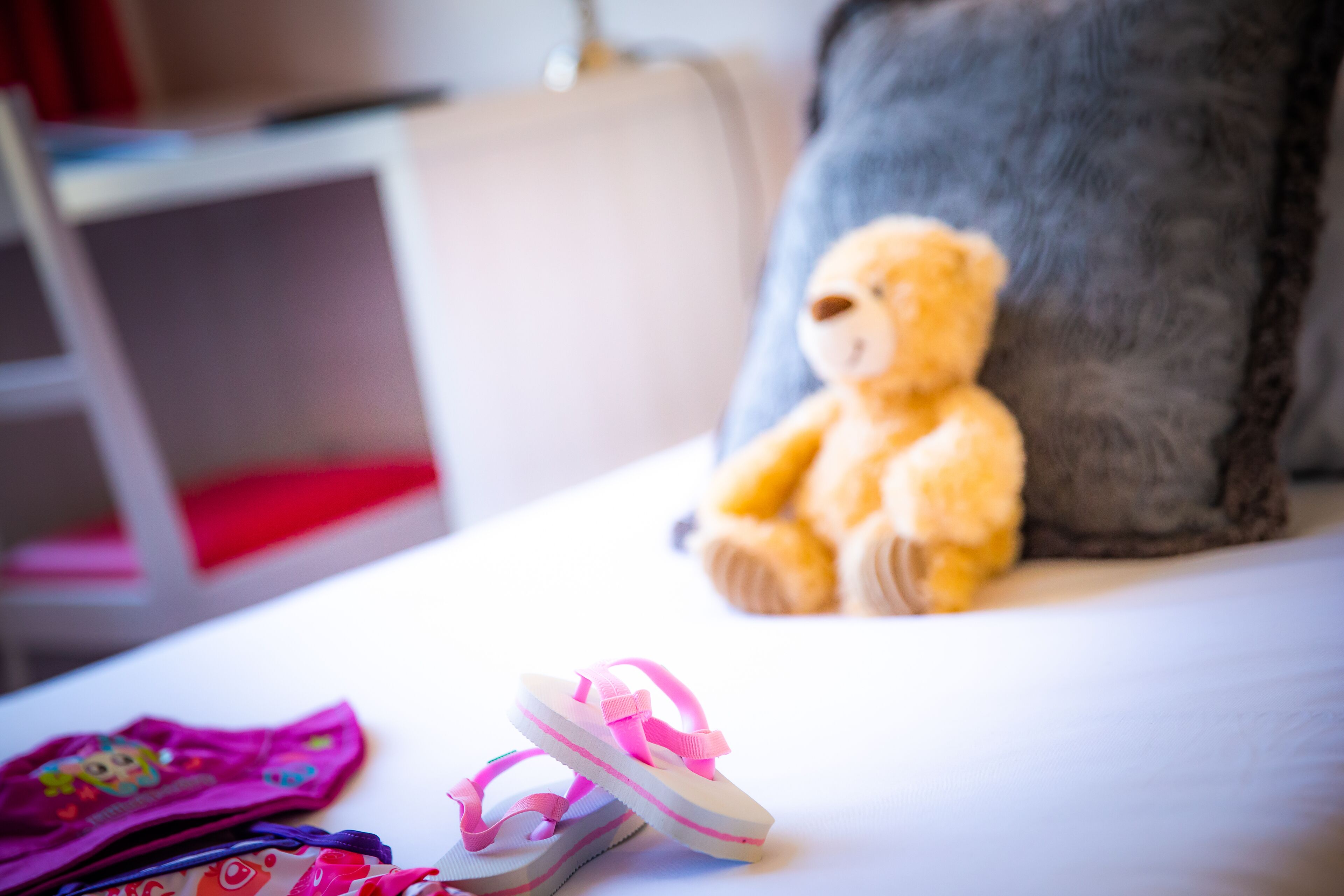 A bed with a teddy bear and pink slippers on it.
