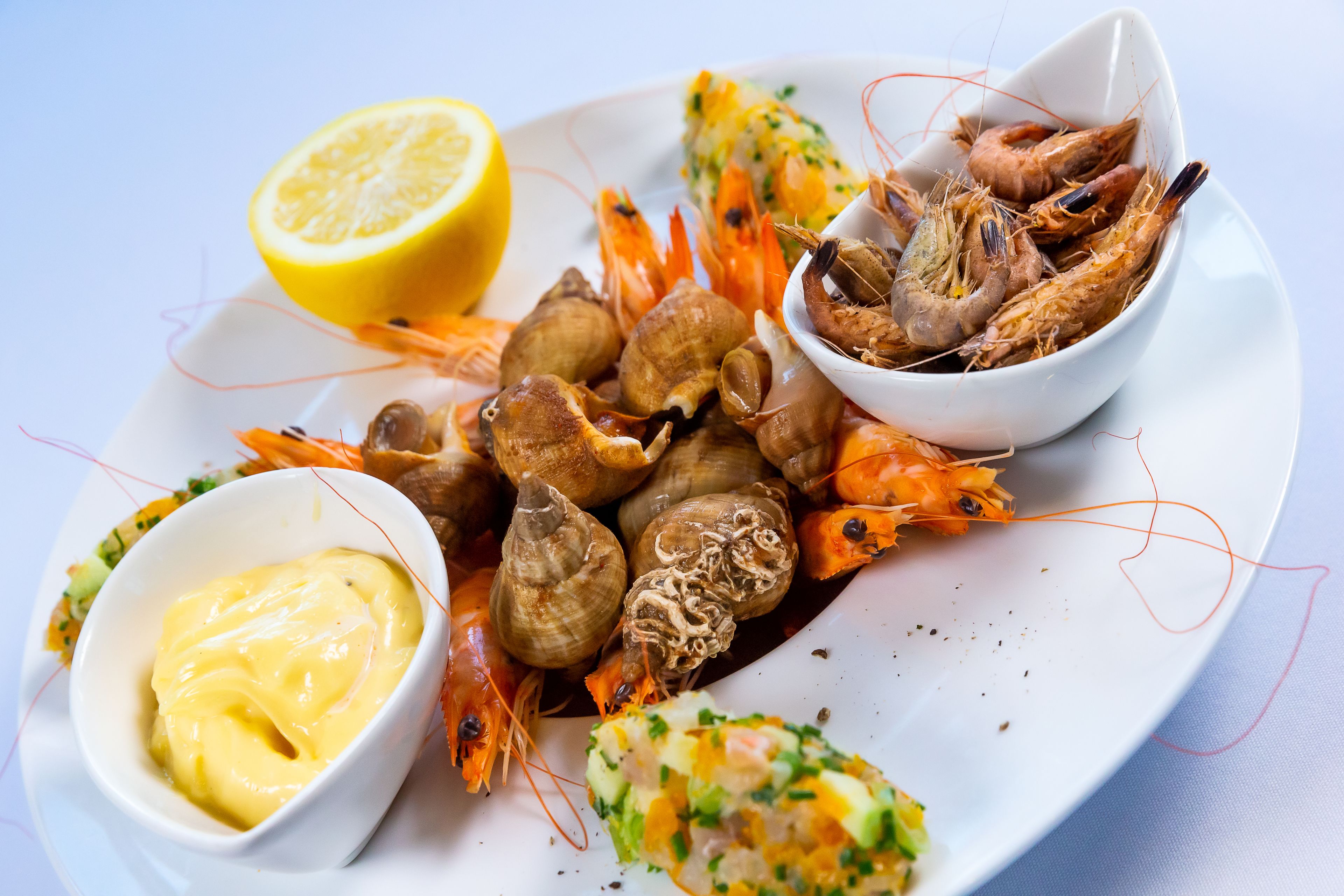 A plate of seafood including shrimp, clams, and mussels, accompanied by lemon and a bowl of sauce.