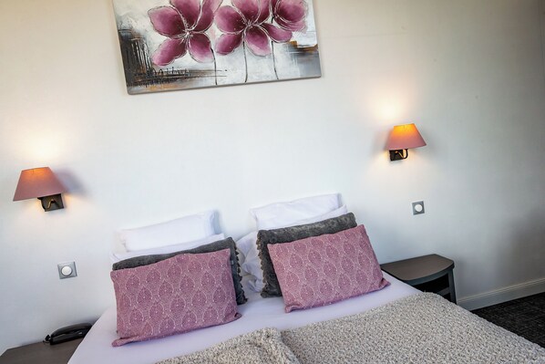 Una habitación de hotel con una cama, dos lámparas de noche, una mesita de noche, un teléfono y un cuadro en la pared.