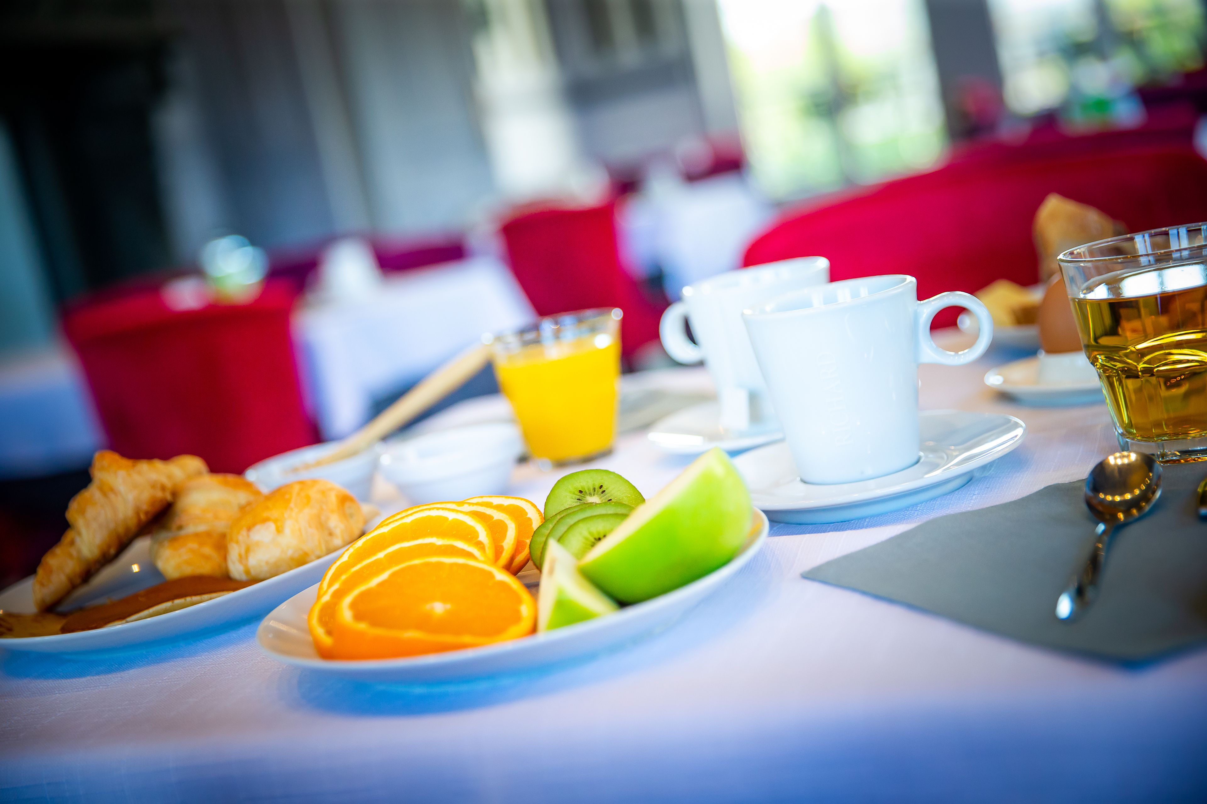 Una mesa de desayuno con croissants, rodajas de naranja, kiwi y un vaso de jugo de naranja.