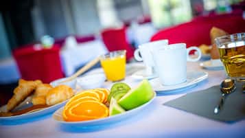 Una mesa de desayuno con croissants, rodajas de naranja, kiwi y un vaso de jugo de naranja.