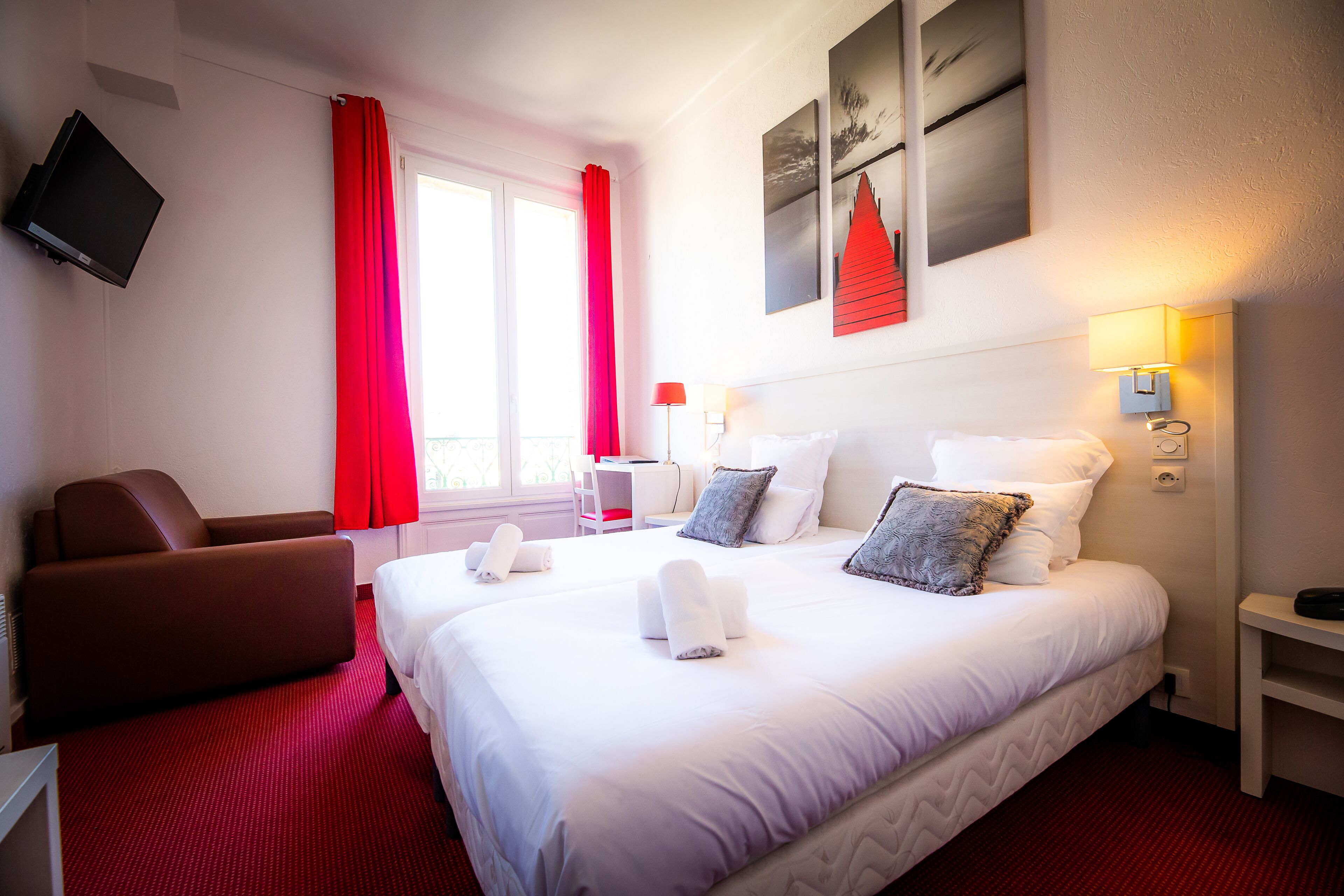 A hotel room with a large bed, a desk, a chair, and a TV mounted on the wall.