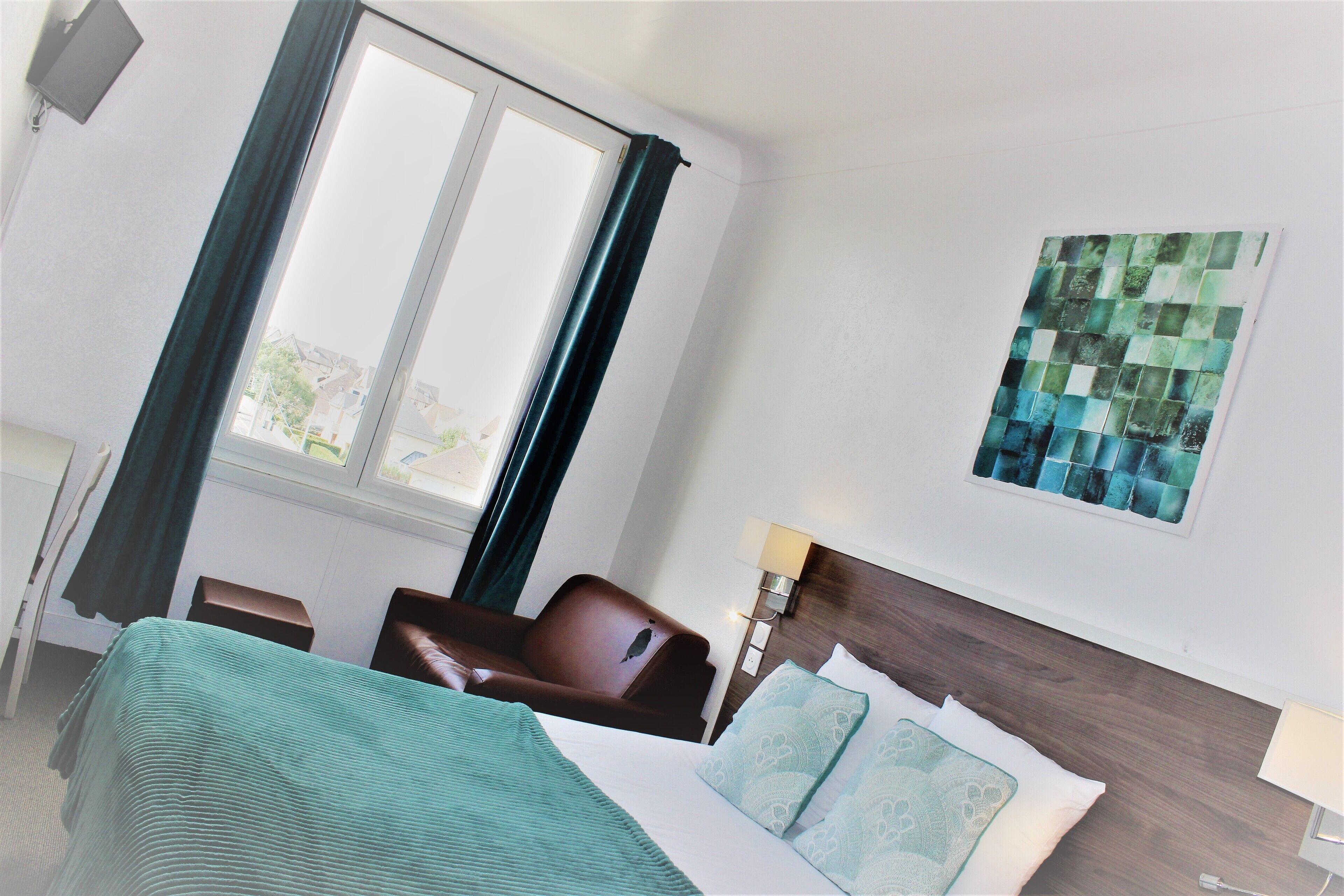 A hotel room with a bed, a chair, a desk, and a window with curtains.