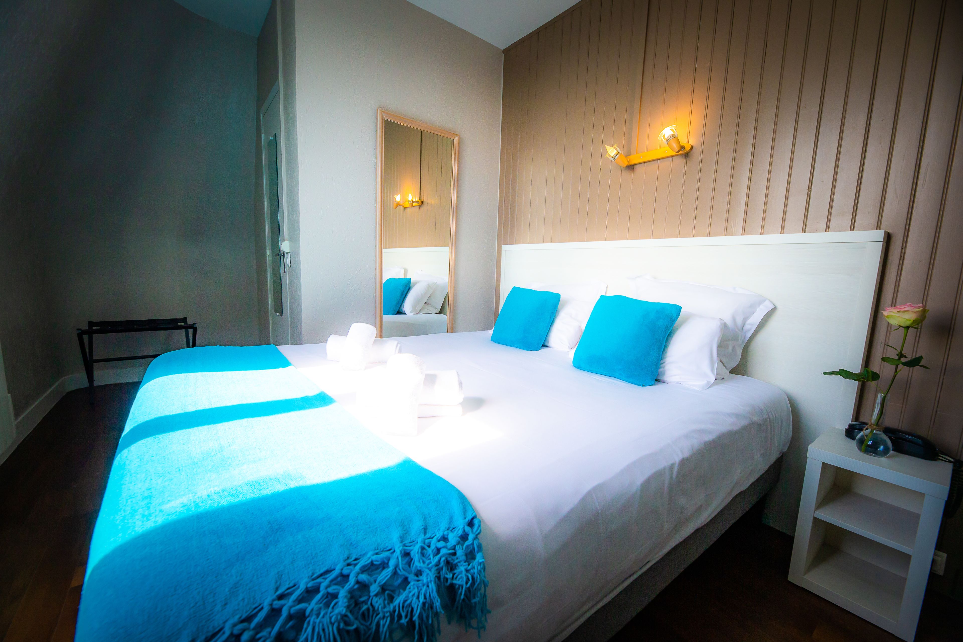 Habitación de hotel con una cama grande, una mesita de noche, un espejo y una lámpara fijada a la pared.