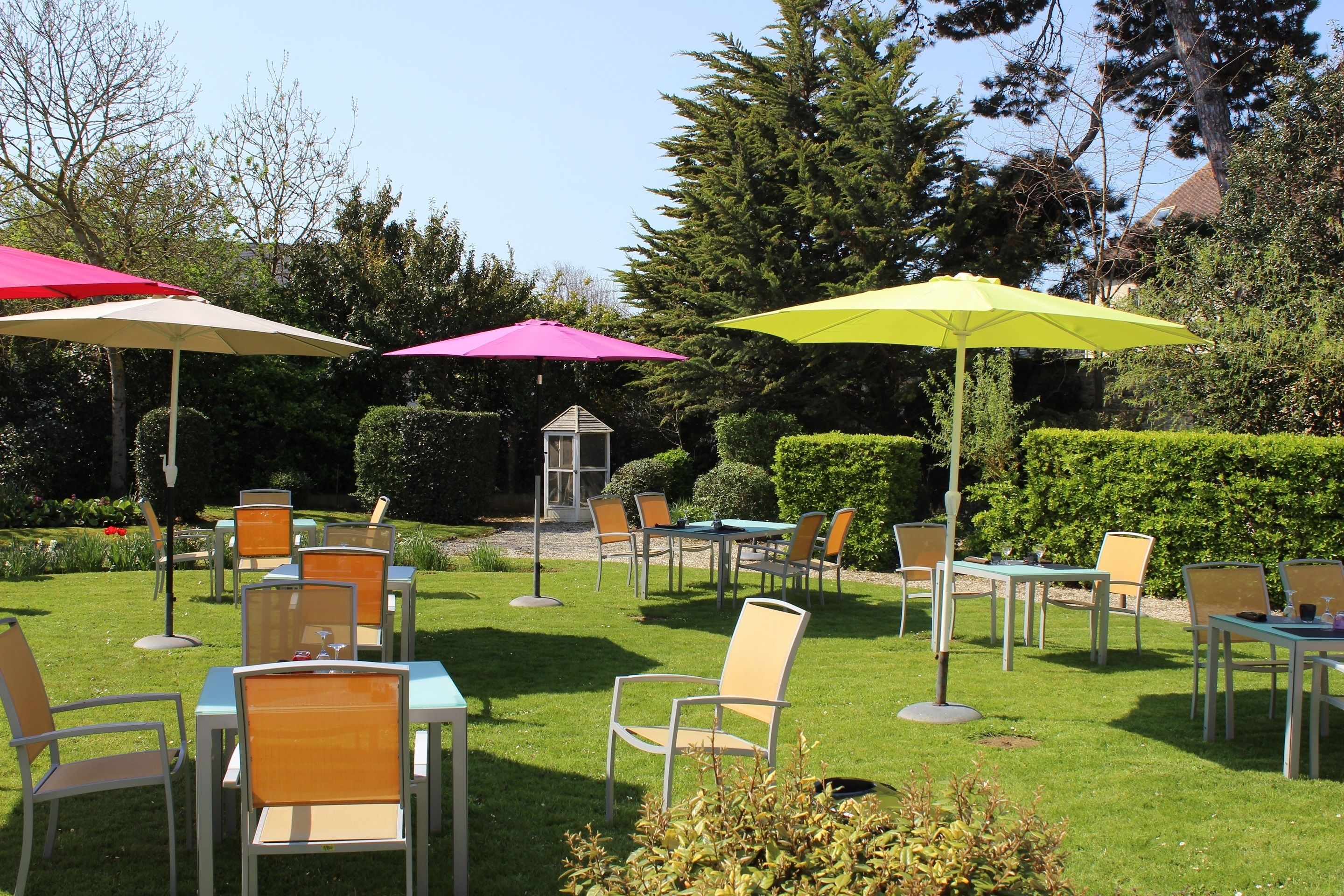 An outdoor seating area with tables and chairs, surrounded by greenery and trees.