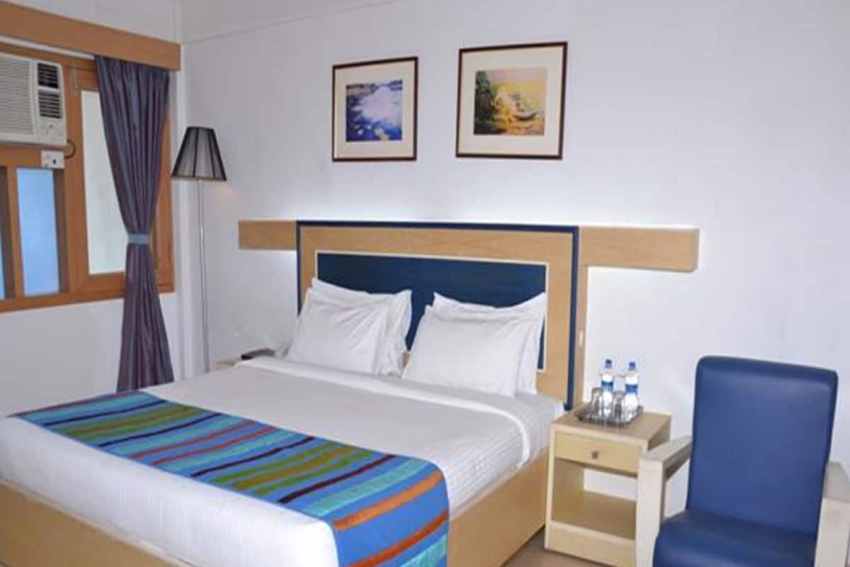 Ein Hotelzimmer mit Bett, Sessel, Nachttisch und zwei gerahmten Bildern an der Wand.