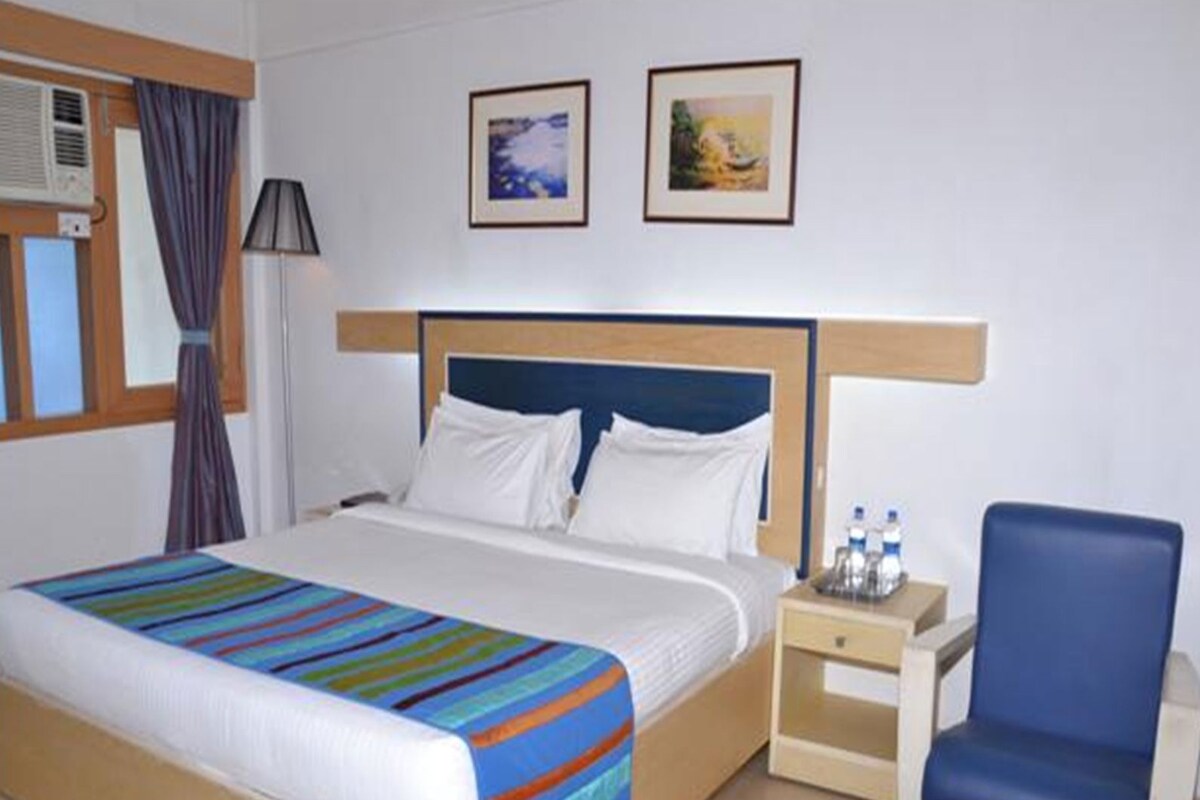 A hotel room with a bed, a chair, a nightstand, and two framed pictures on the wall.