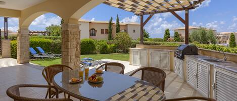 Un patio al aire libre con una mesa de comedor, sillas y zona de barbacoa.