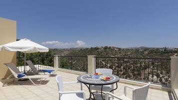 Una terraza con una mesa y sillas, una sombrilla y una vista panorámica de un paisaje montañoso.