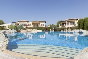 A swimming pool with a clear blue water surface, surrounded by a paved deck and large rocks.