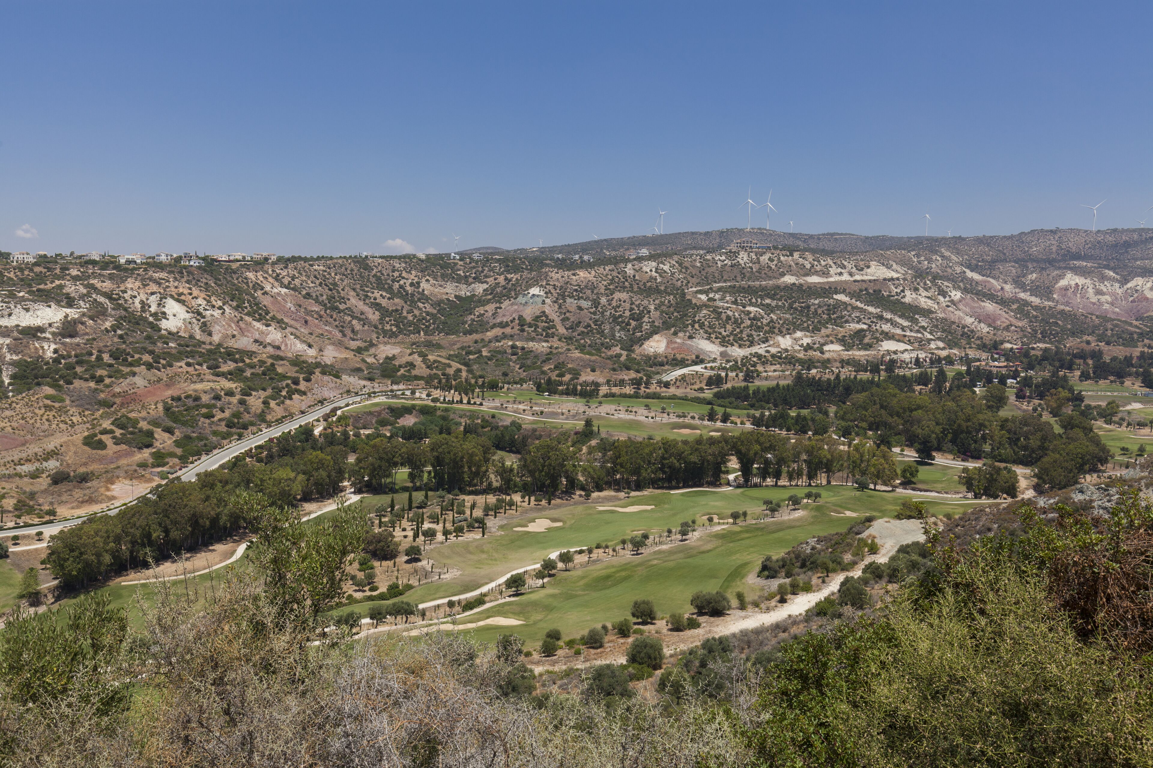 A mountainous landscape with a golf course, wind turbines, and a winding road.