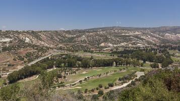 A mountainous landscape with a golf course, wind turbines, and a winding road.