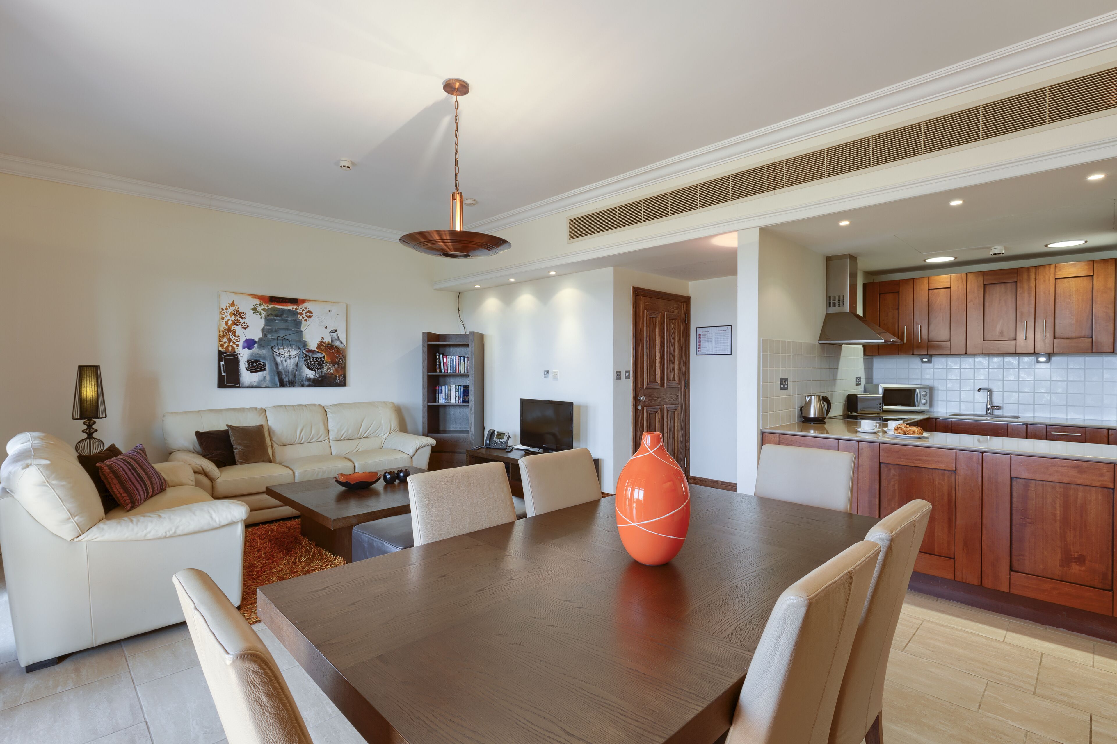 Una sala de estar moderna con una mesa de comedor, sofá y una cocina con armarios de madera y un microondas.