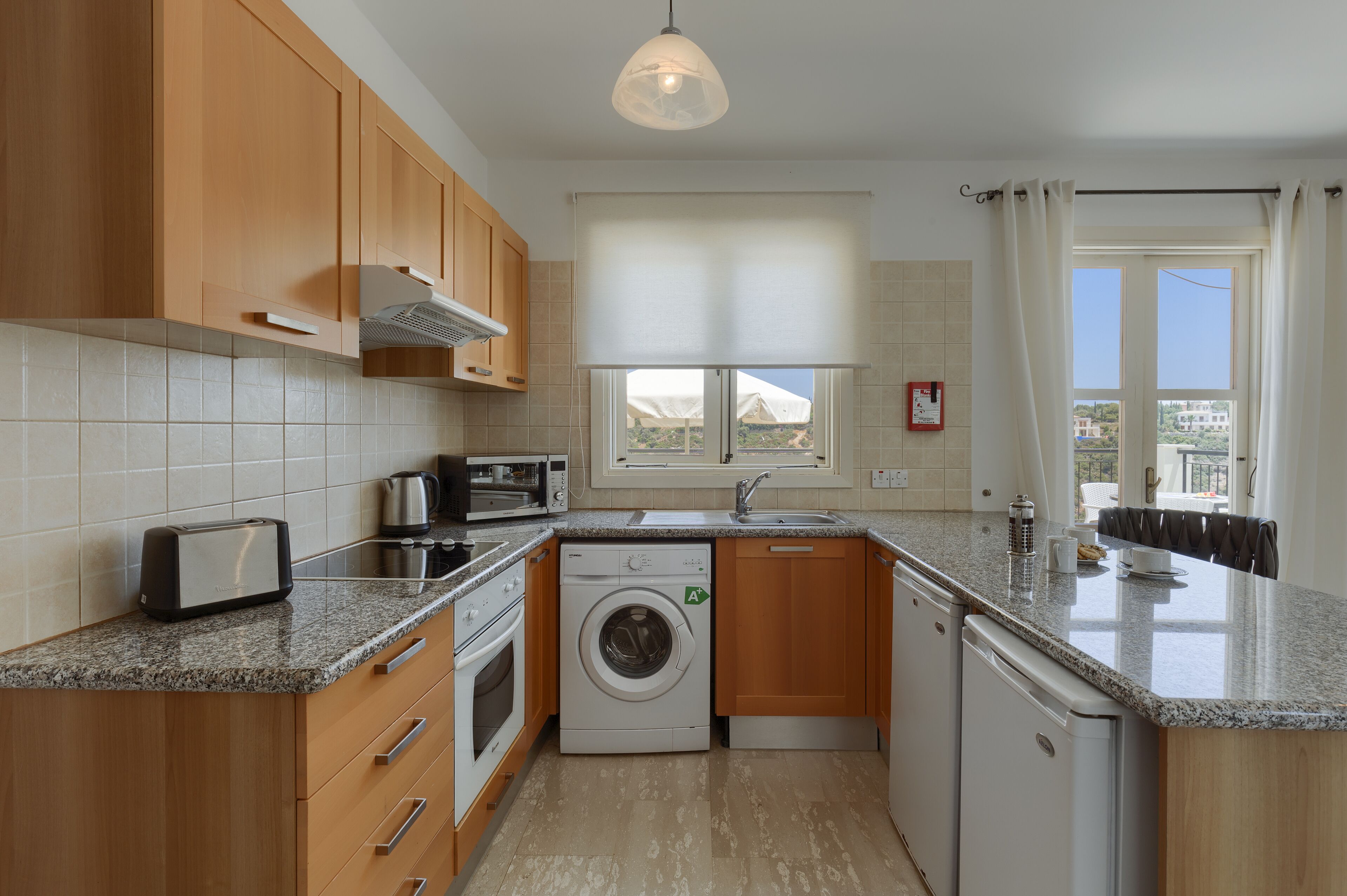 A compact kitchen with wooden cabinets, a built-in washing machine, a microwave, and a toaster.