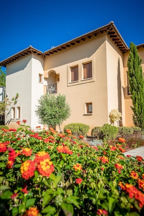 A two-story house with a 'For Sale' sign, surrounded by well-maintained gardens and a clear blue sky. - Aphrodite Hills Rentals – Apartments (Kouklia)