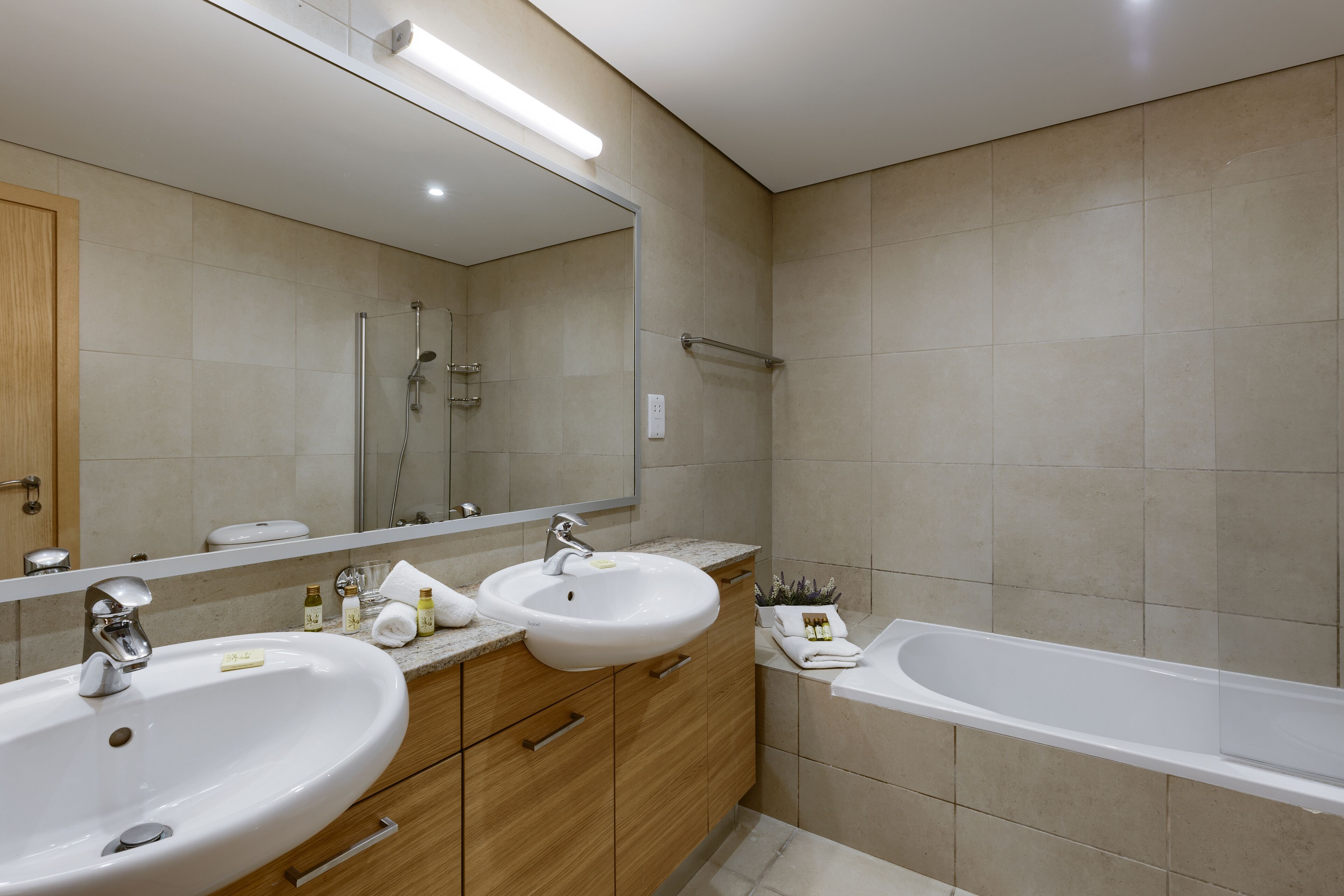 A modern bathroom with two sinks, a bathtub, and a large mirror.