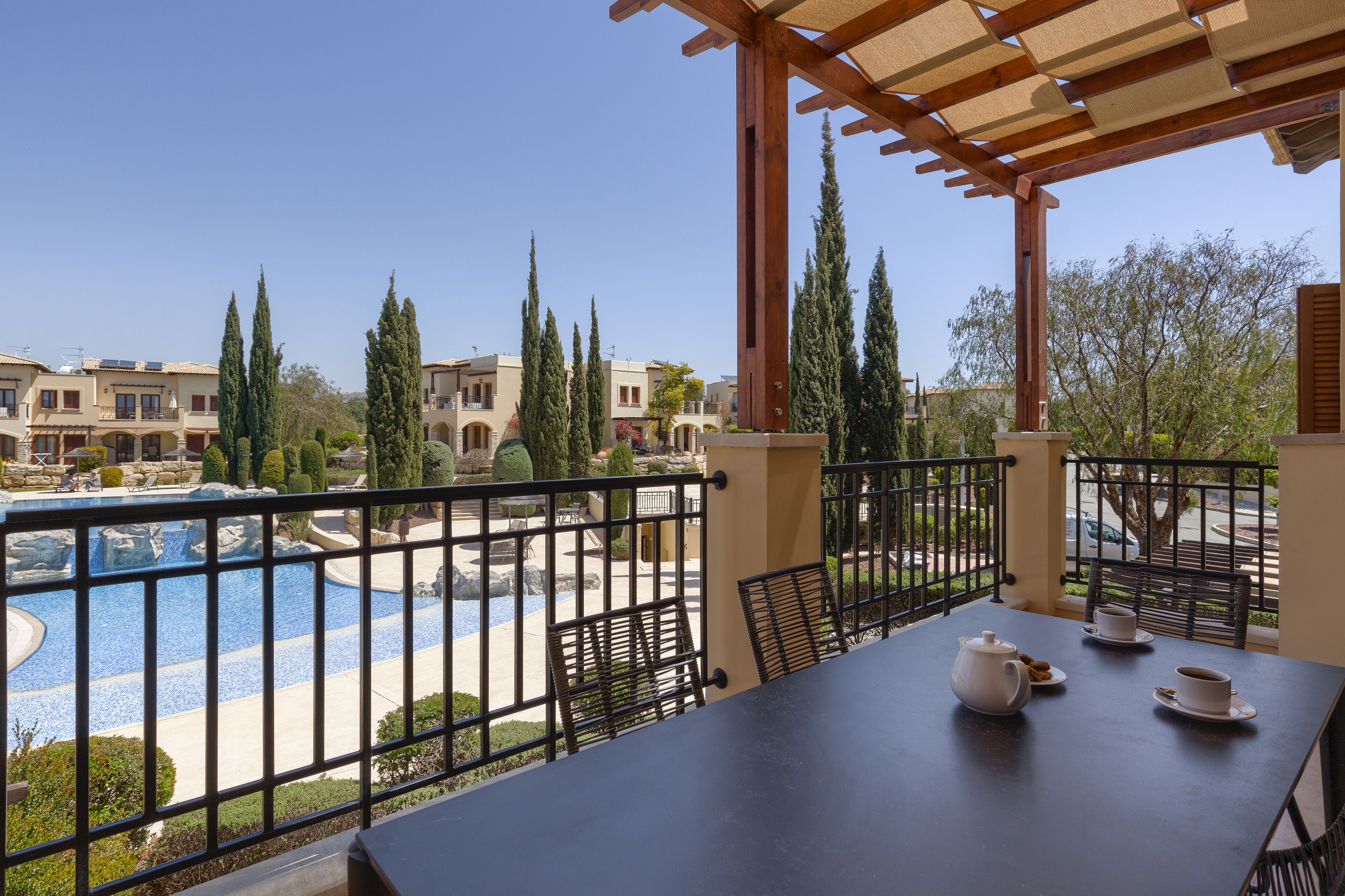 Un balcon avec une table préparée pour le thé, donnant sur une piscine et un jardin aménagé.