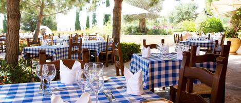 An outdoor dining area with checkered tablecloths, wooden chairs, and neatly set tables with cutlery and glasses.