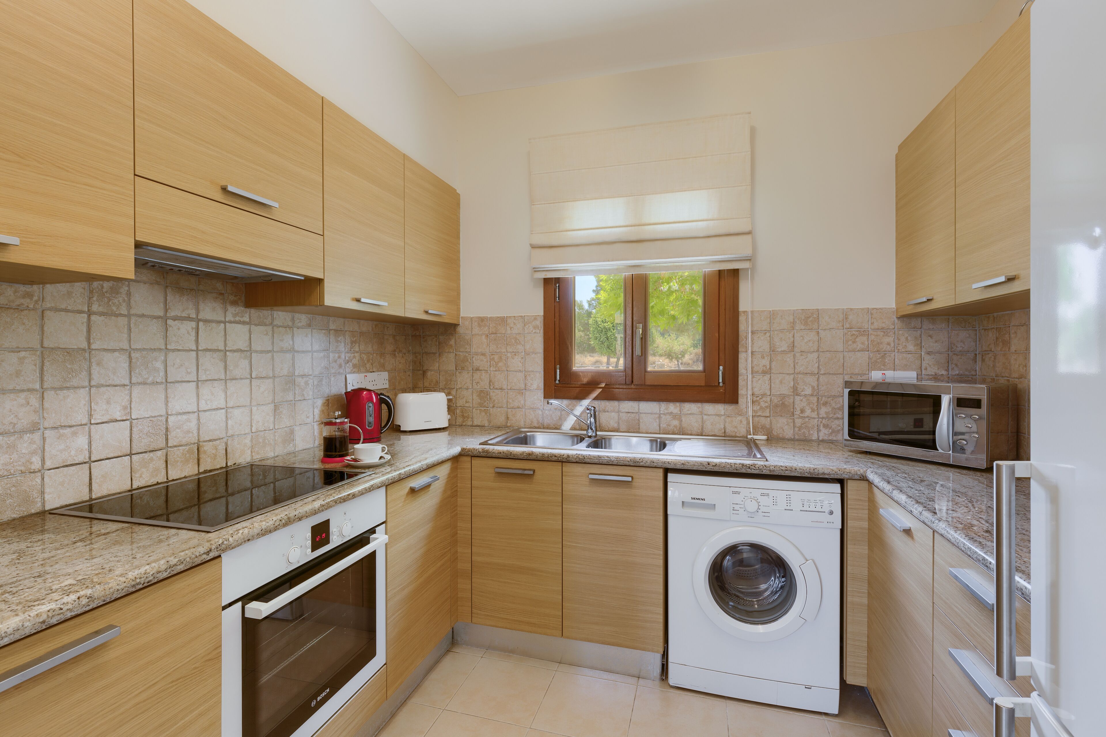 Une cuisine moderne avec des meubles en bois, un four encastré, un lave-linge, un four à micro-ondes et une fenêtre qui laisse entrer la lumière naturelle.