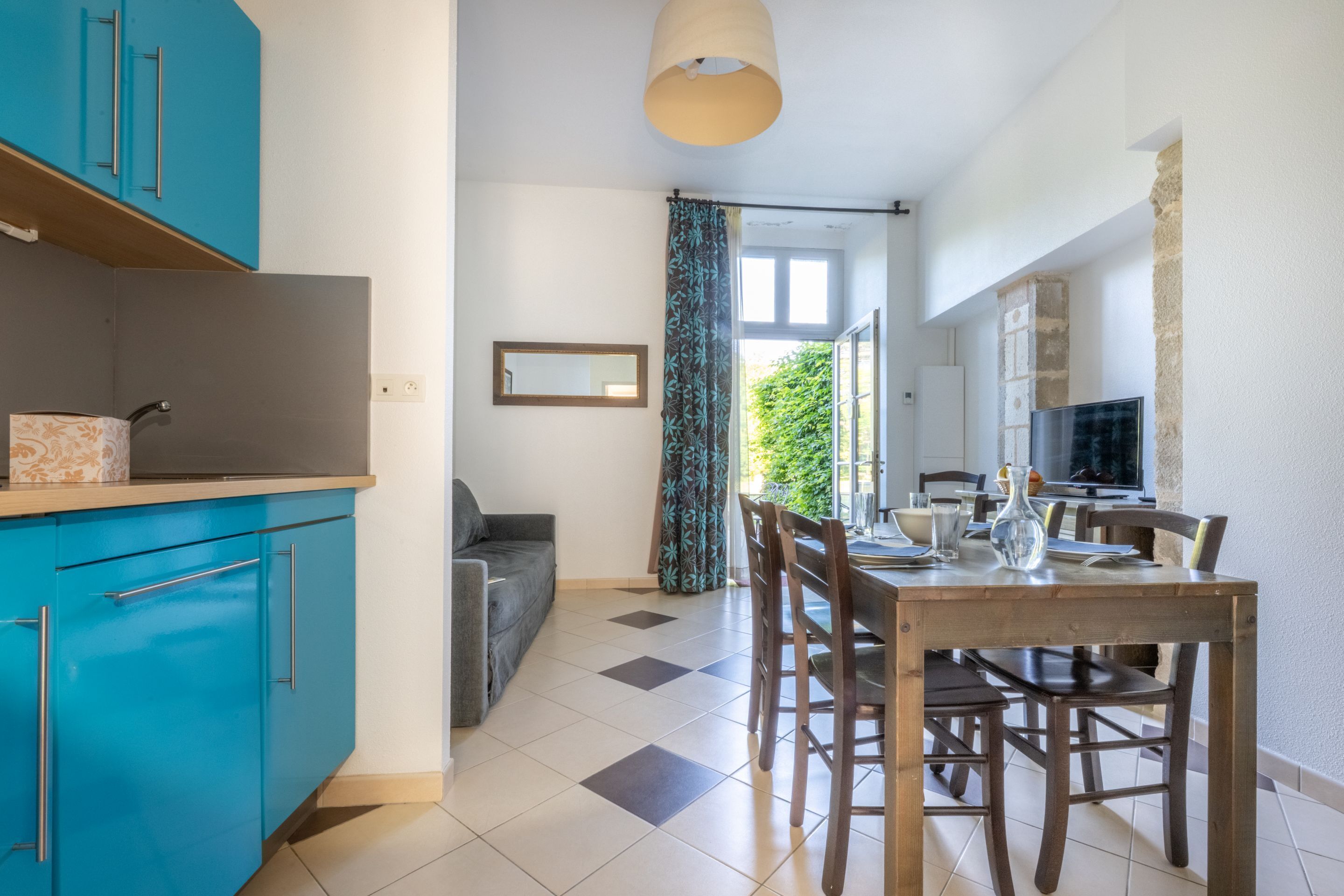 Una cocina moderna con armarios azules, un comedor con sillas de madera y un ventanal con cortinas.