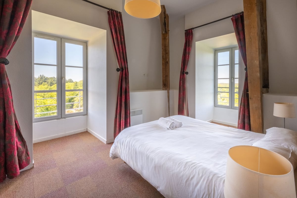 Un dormitorio con una cama grande, dos ventanas y vistas a zonas verdes.