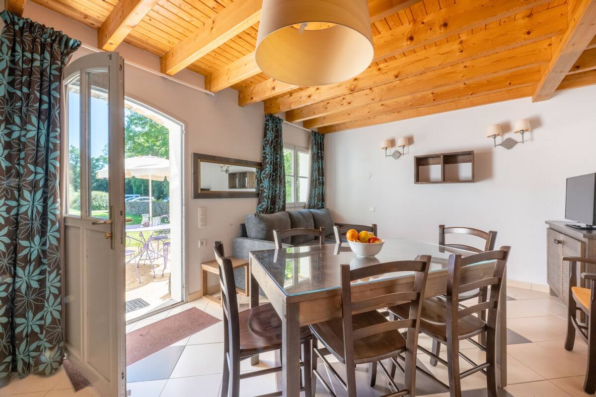 Un comedor con una mesa de vidrio, sillas de madera, un cuenco de fruta y un sofá.