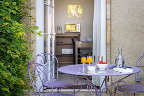 Un tavolo con sedie, una ciotola di frutta, bicchieri e un libro su un patio che si affaccia su una stanza con TV e scaffali.