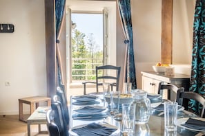 Un coin repas avec une table dressée pour quatre personnes, une fenêtre avec des rideaux et une vue sur la verdure à l’extérieur.