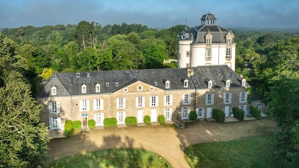 Ein großes, historisches Gebäude mit zahlreichen Fenstern und einem markanten Turm, umgeben von üppigem Grün.