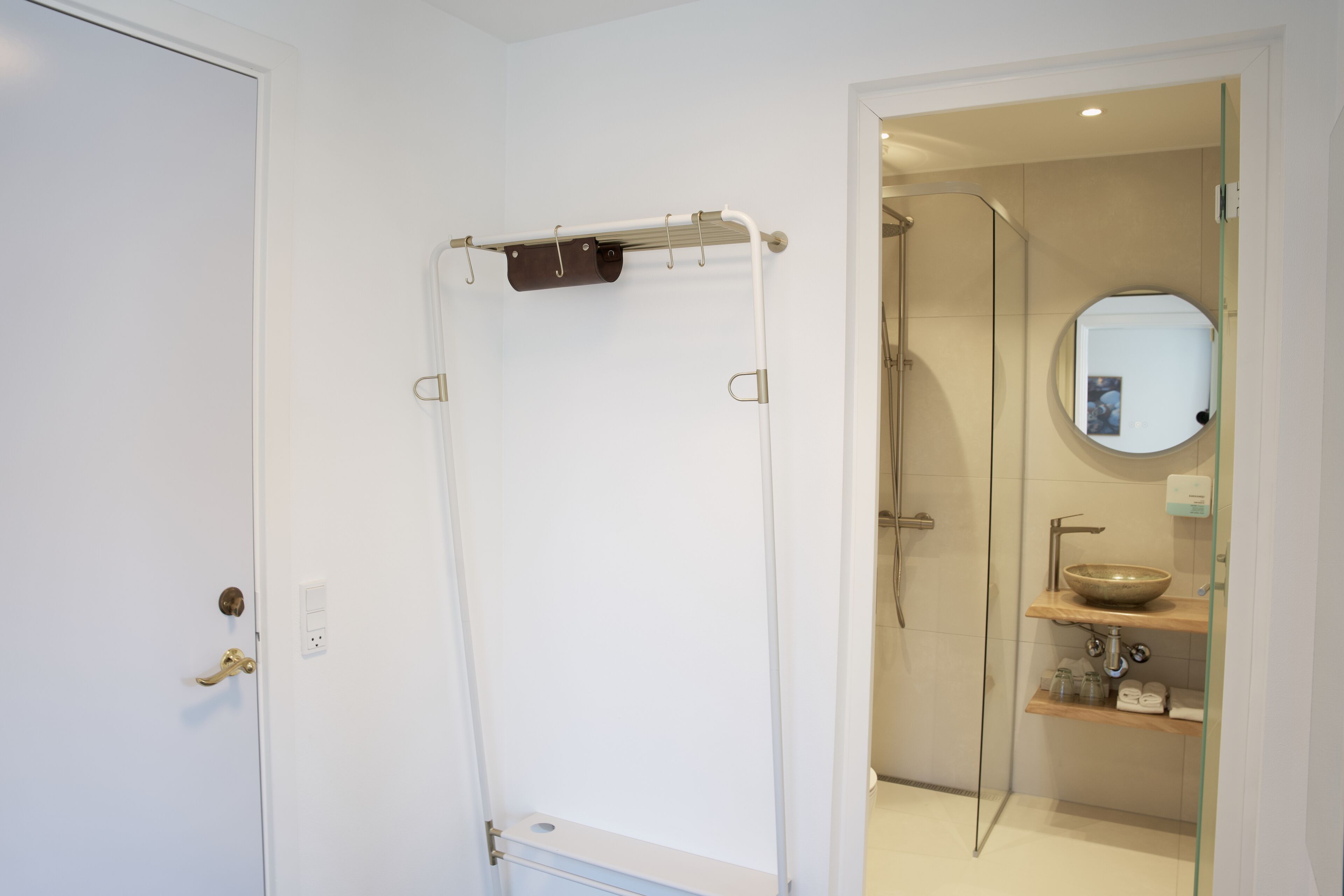 A bathroom with a glass shower enclosure, a white door with a brass handle, and a mirror above a wooden shelf with a bowl sink.
