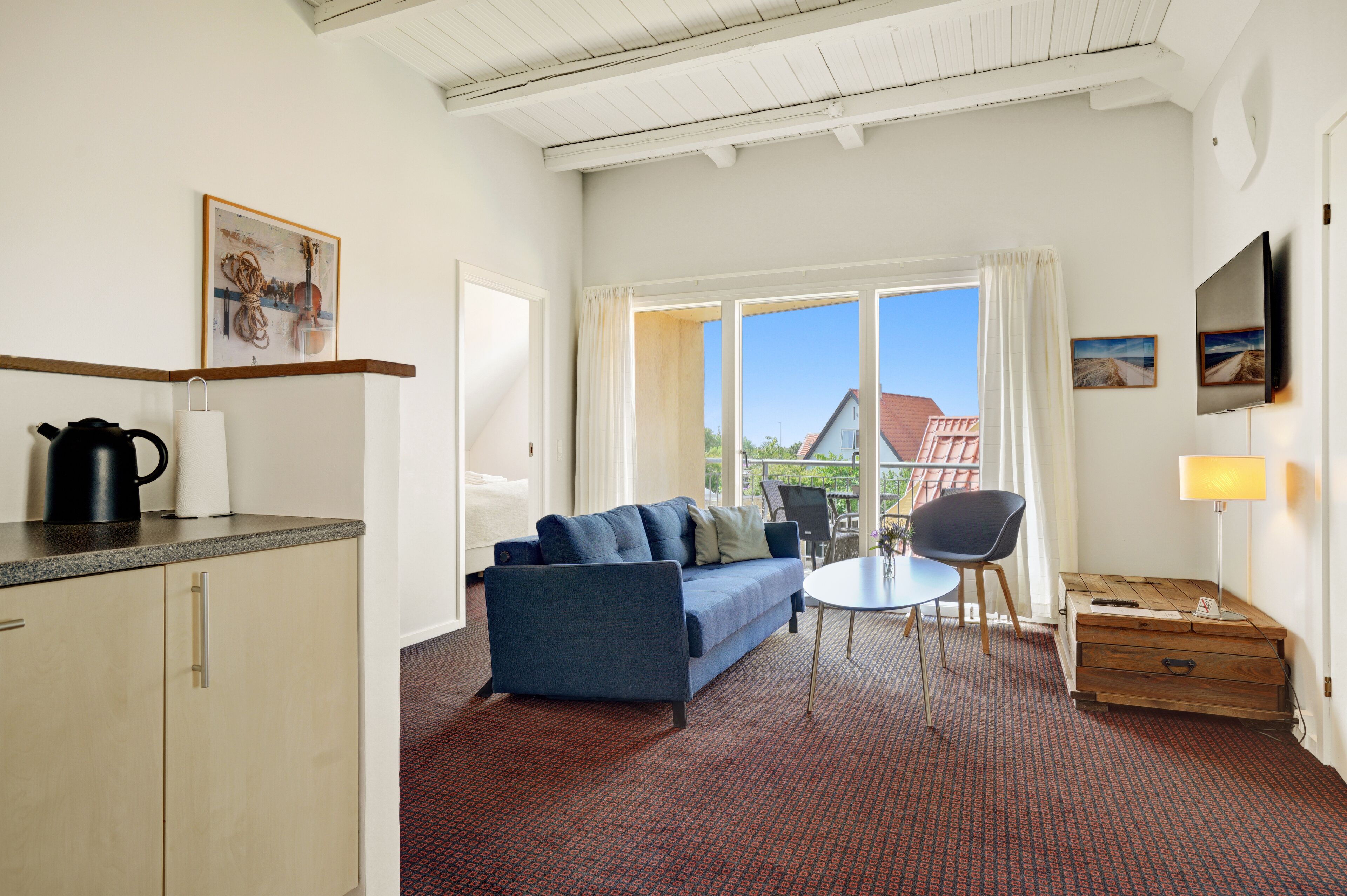 A modern room with a blue sofa, a small table, a TV, and a window with a view of a house.