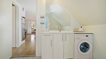 A laundry room with a Bosch washing machine, a countertop with a mirror, and a door leading to another room.