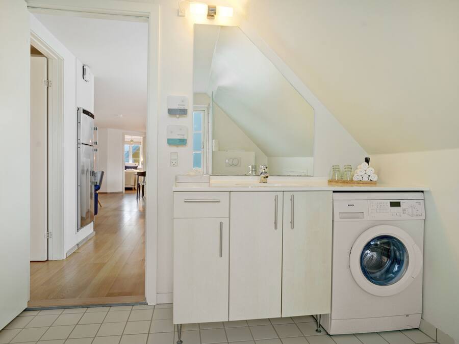 A laundry room with a Bosch washing machine, a countertop with a mirror, and a door leading to another room.