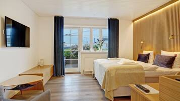 A hotel room with a bed, a desk, a chair, a TV mounted on the wall, and a window with curtains.