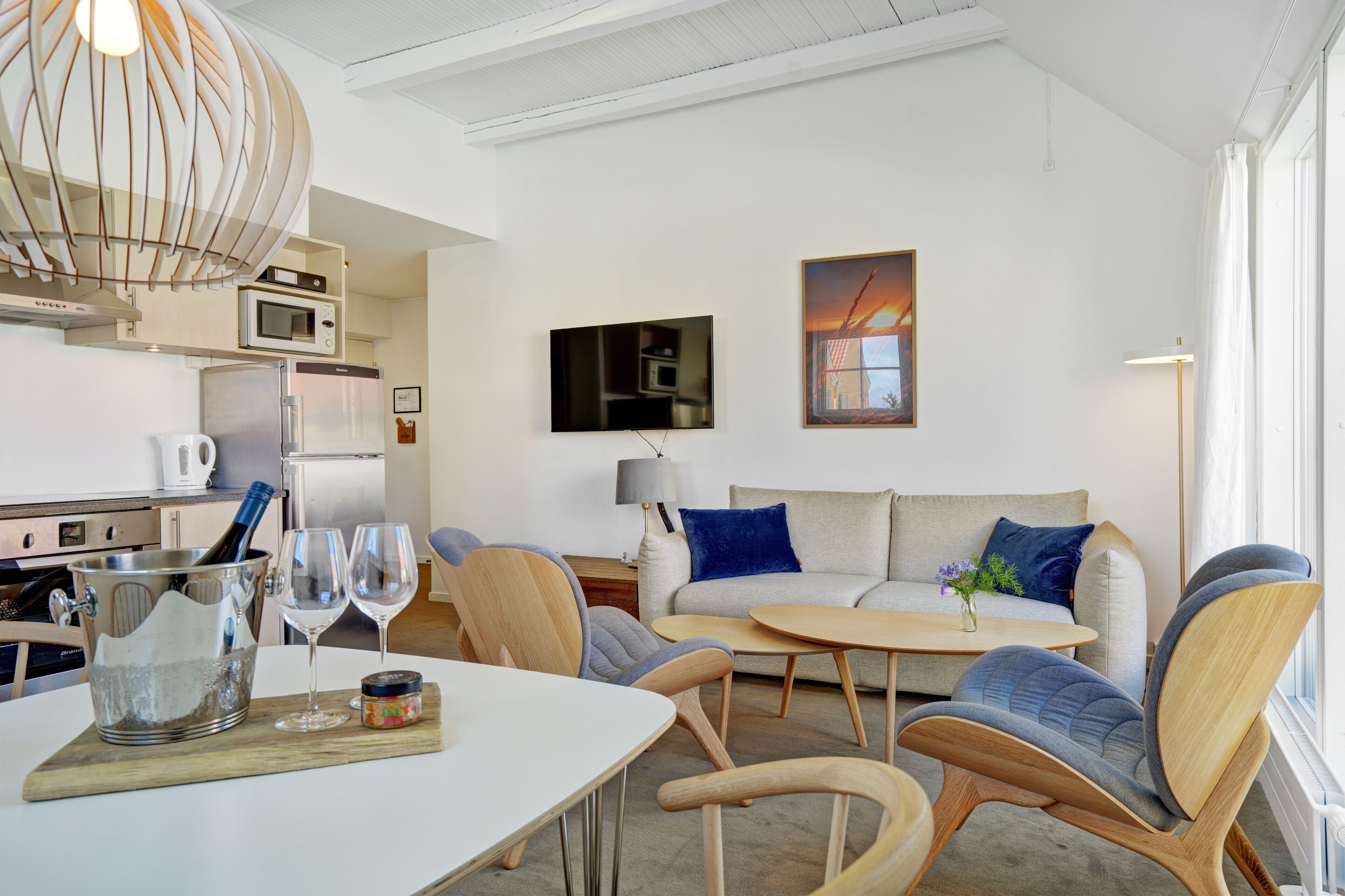 Una sala de estar moderna con un sofá, dos sillones, una mesa de centro y una mesa de comedor con una copa de vino y una botella.