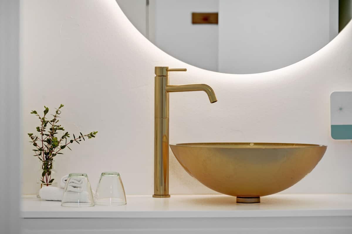 Een badkamer met een gouden kraan, een grote wasbak en een spiegel met een gebogen lijst.