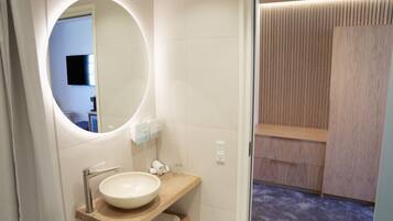 Un baño moderno con un espejo redondo, un mueble de tocador de madera, un lavabo y una zona de ducha con paneles de madera.