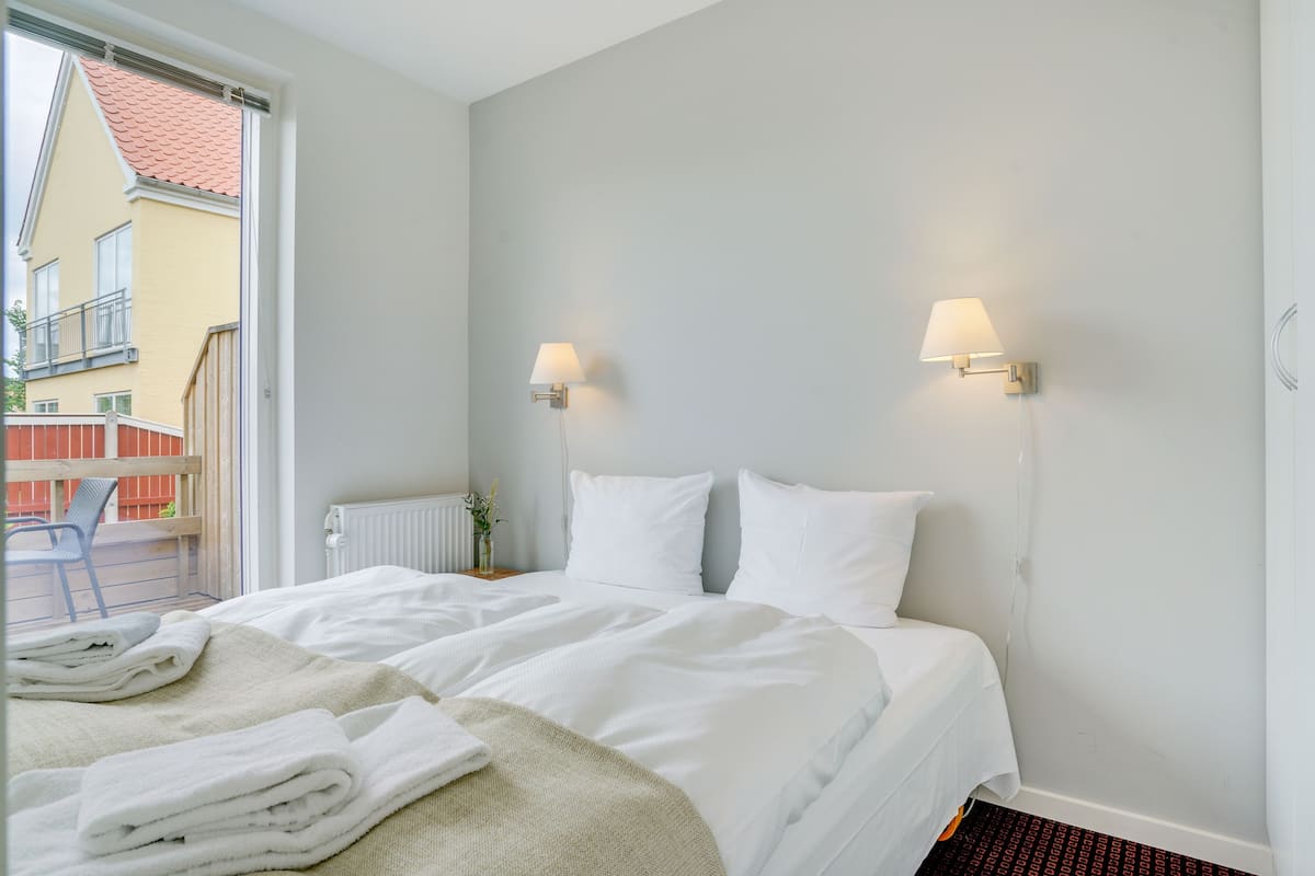 Hotelkamer met een bed, twee wandlampen, een radiator en uitzicht op een gebouw.