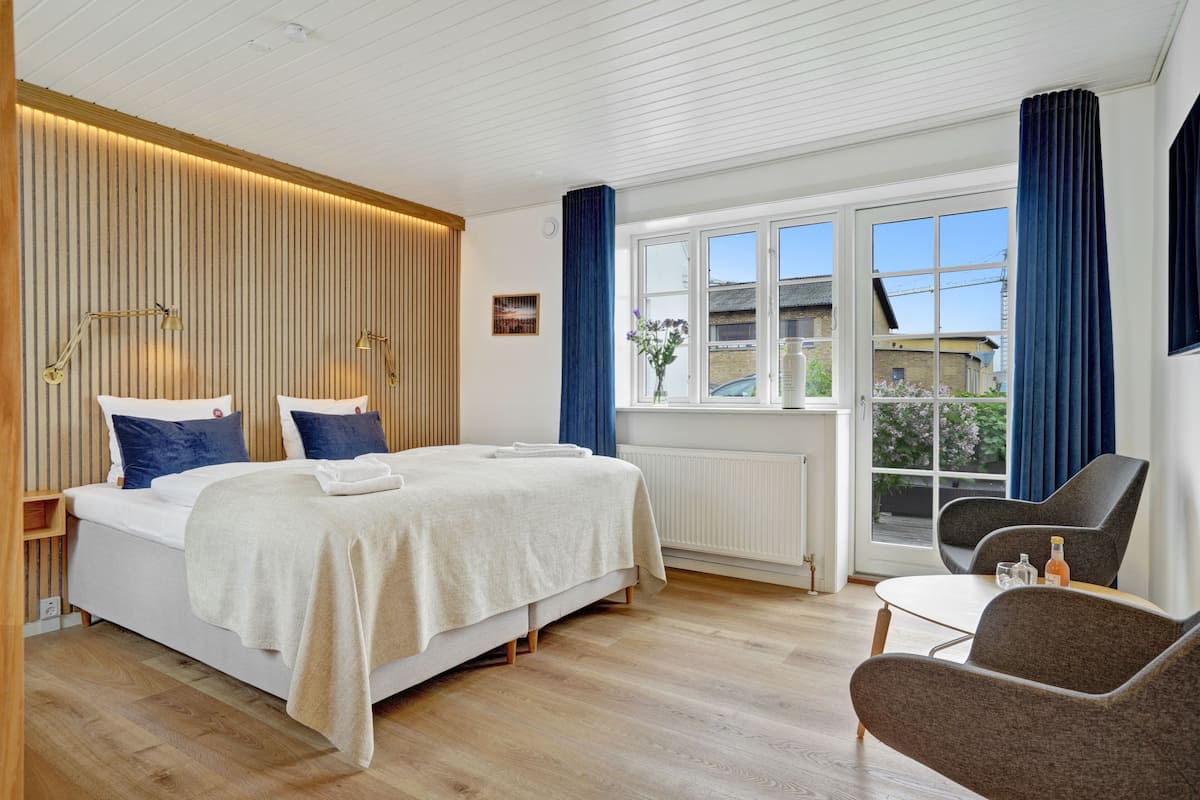 Een moderne hotelkamer met een groot bed, een zithoek met een tafel en stoelen, een raam met gordijnen en uitzicht op buiten.