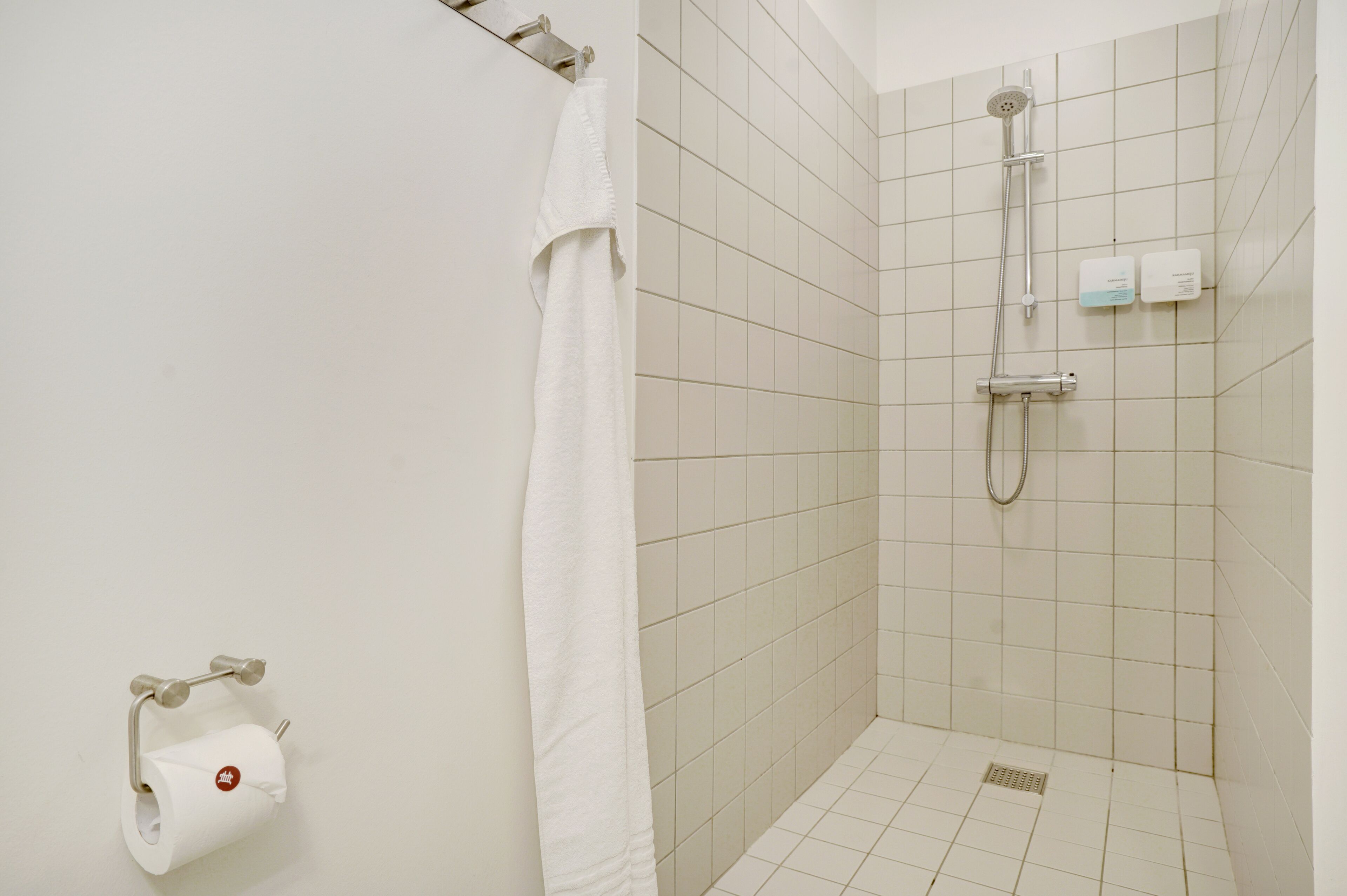 A small, tiled shower area with a toilet paper holder and a towel rack.