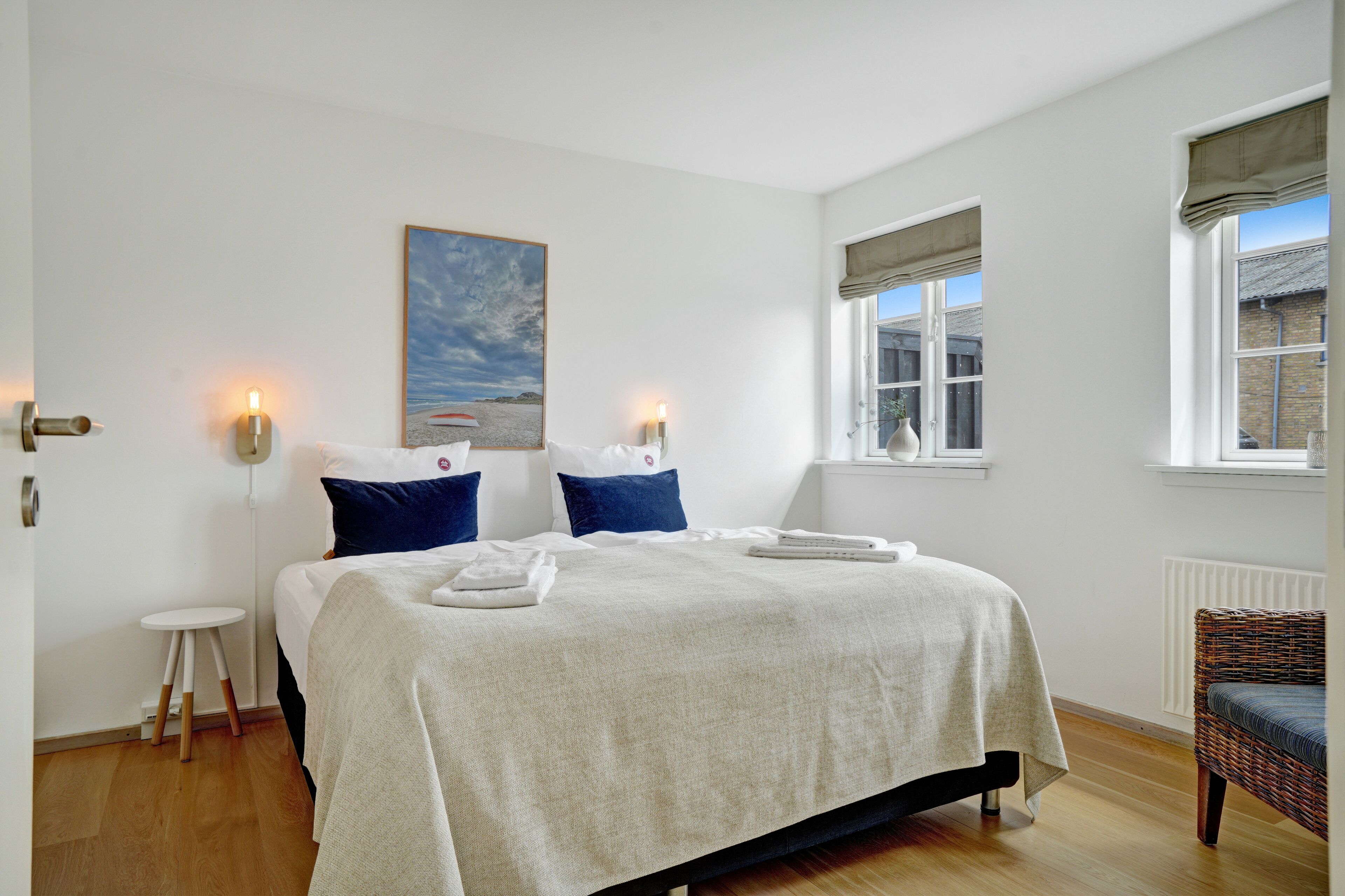 A neatly arranged bedroom with a bed, bedside lamps, a small table, and a chair.