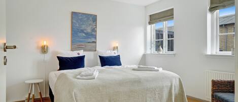 A neatly arranged bedroom with a bed, bedside lamps, a small table, and a chair.