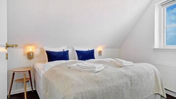 Una cama bien hecha con ropa de cama blanca y azul, una mesita de madera y una lámpara de pared.