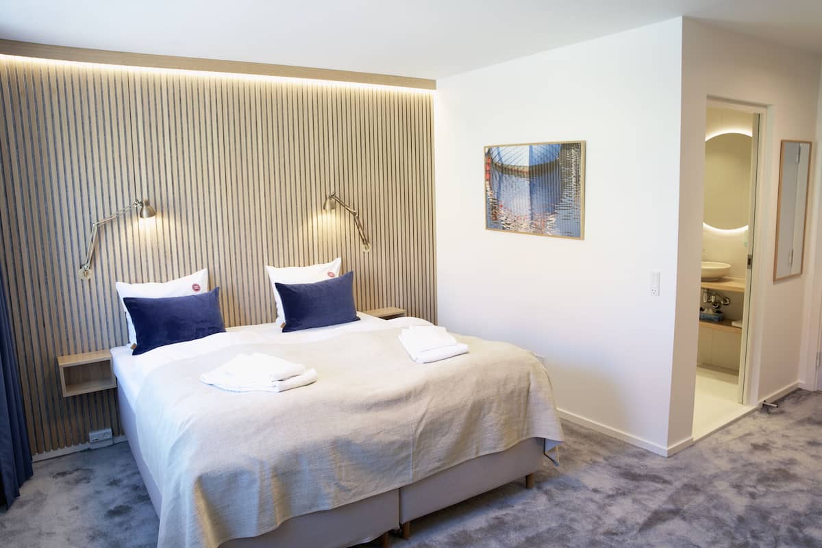 Een moderne hotelkamer met een groot bed, twee bedlampen, een klein nachtkastje en een aan de muur bevestigd kunstwerk.