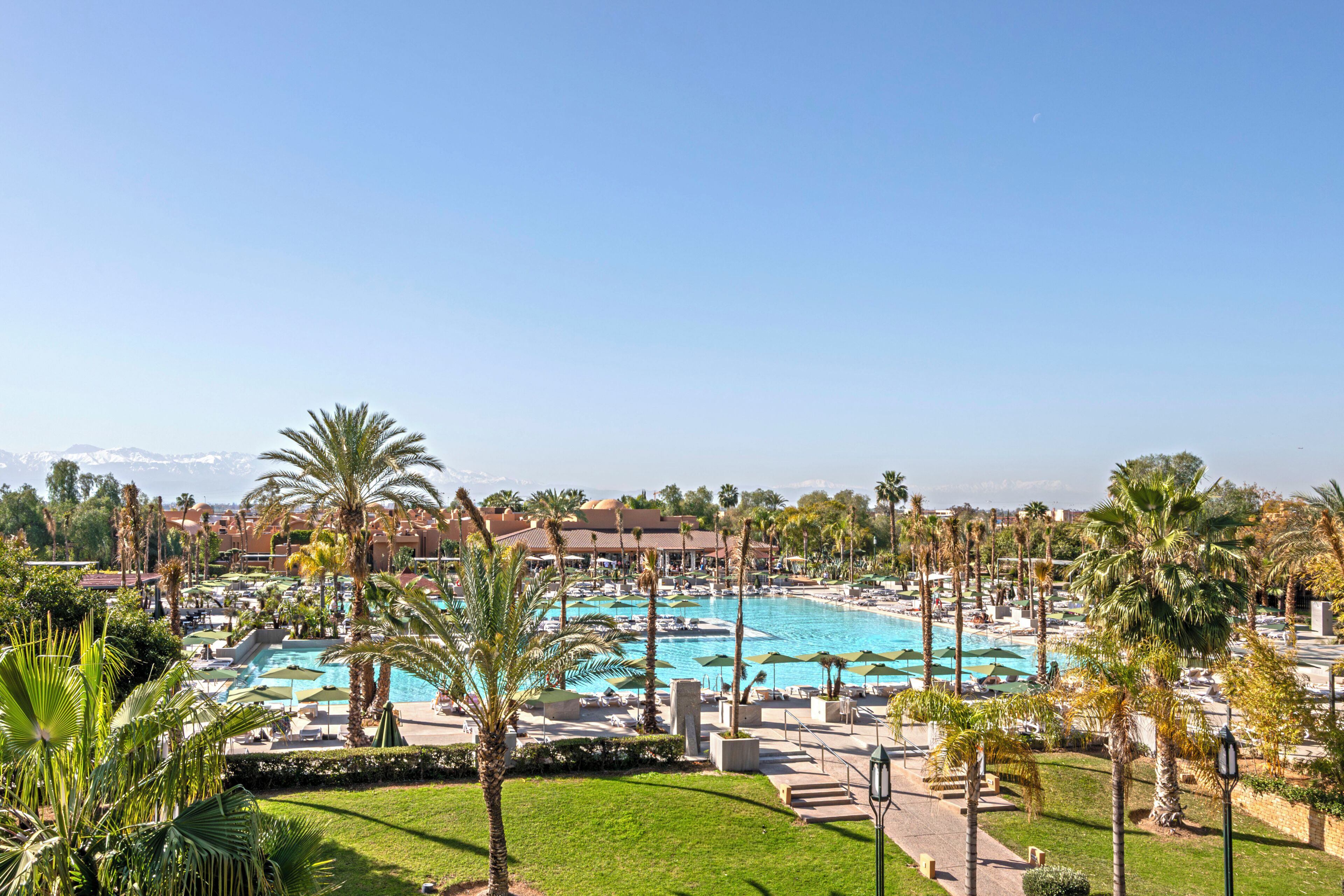 Un resort con una amplia zona de piscina, palmeras y vistas a montañas distantes.