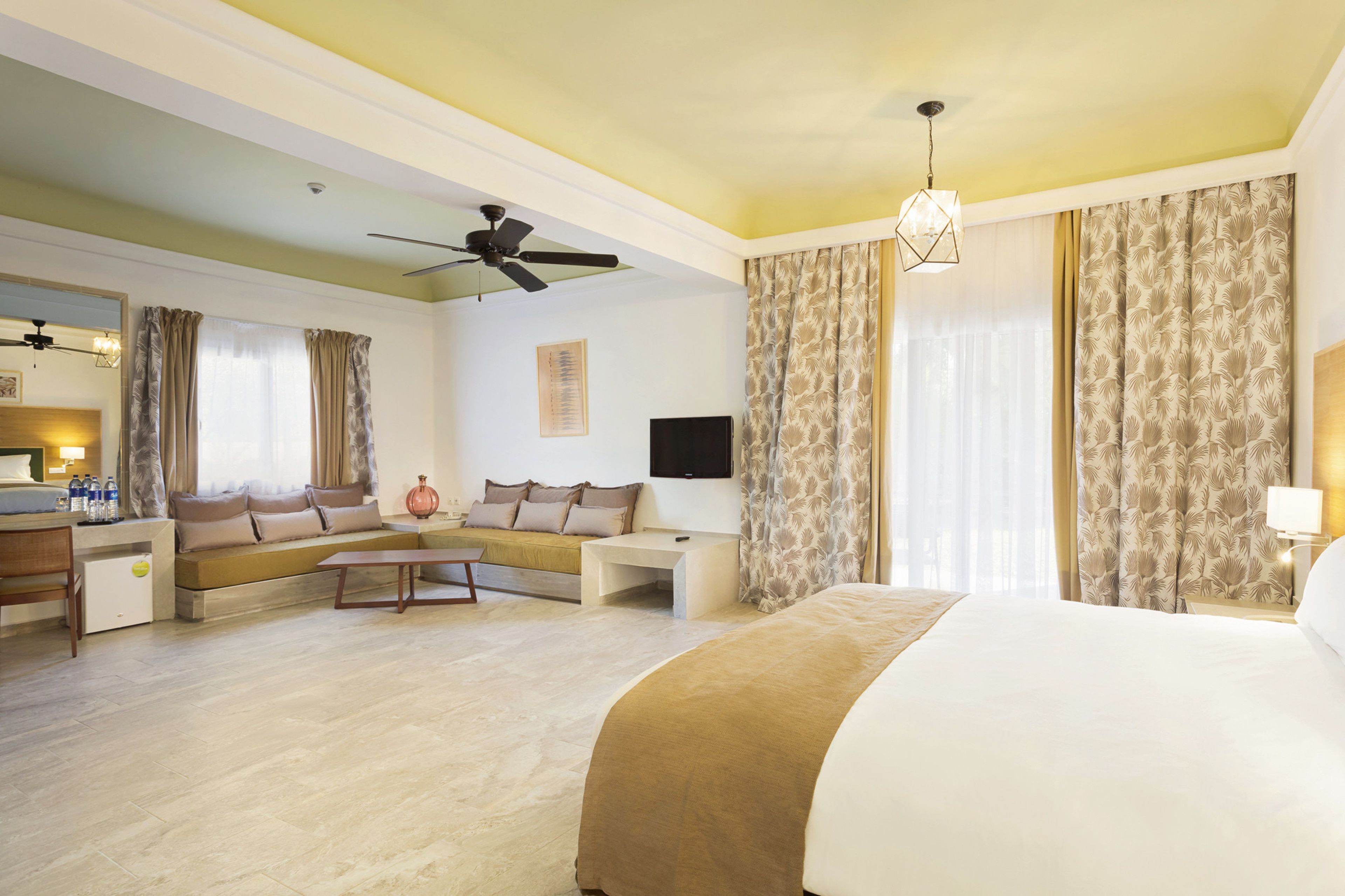 A hotel room with a bed, a sofa, a desk, a ceiling fan, and curtains.