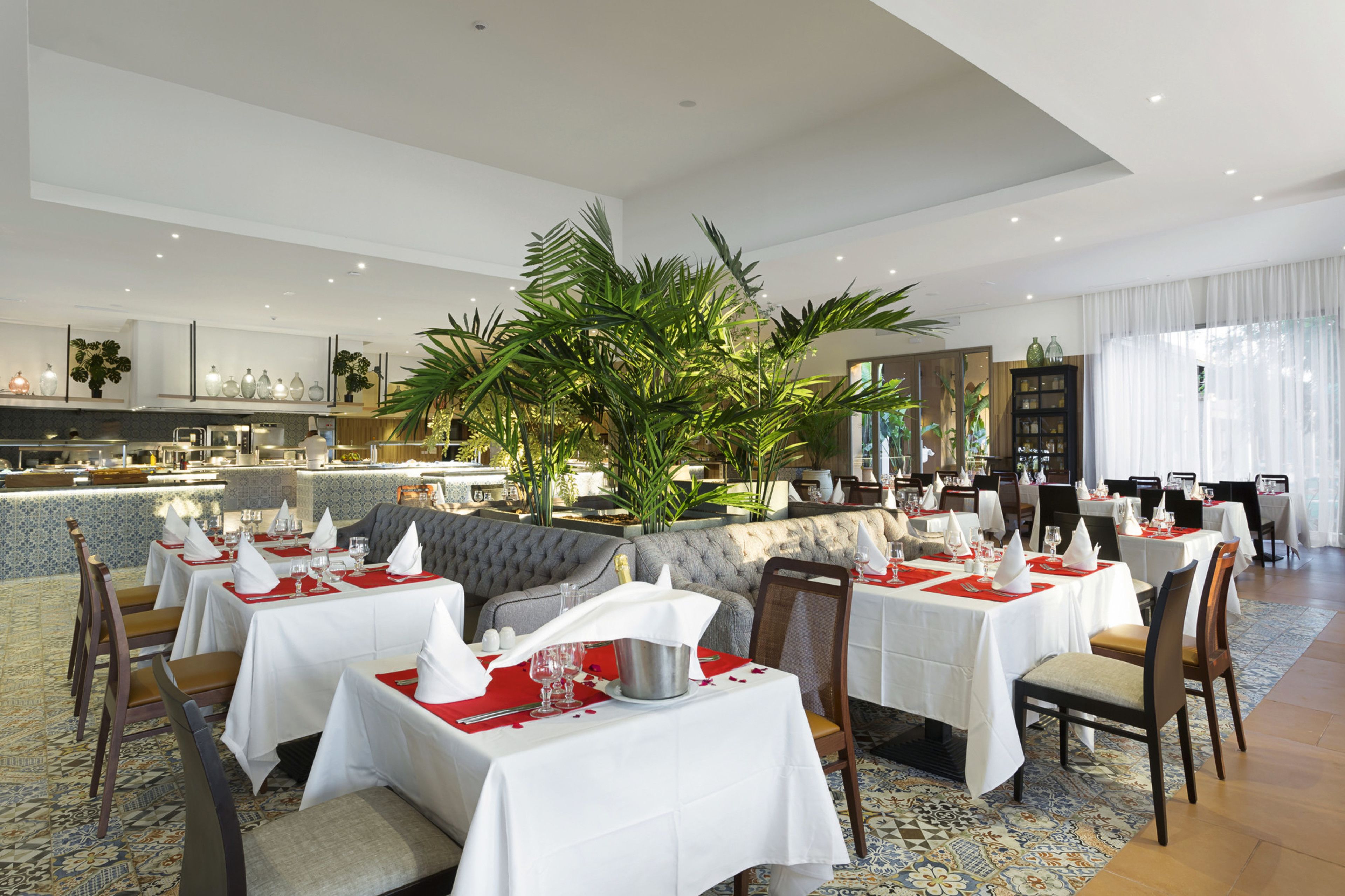 A restaurant with white tablecloths, red placemats, and a large potted plant in the center.