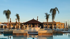A resort pool area with lounge chairs, umbrellas, and palm trees.