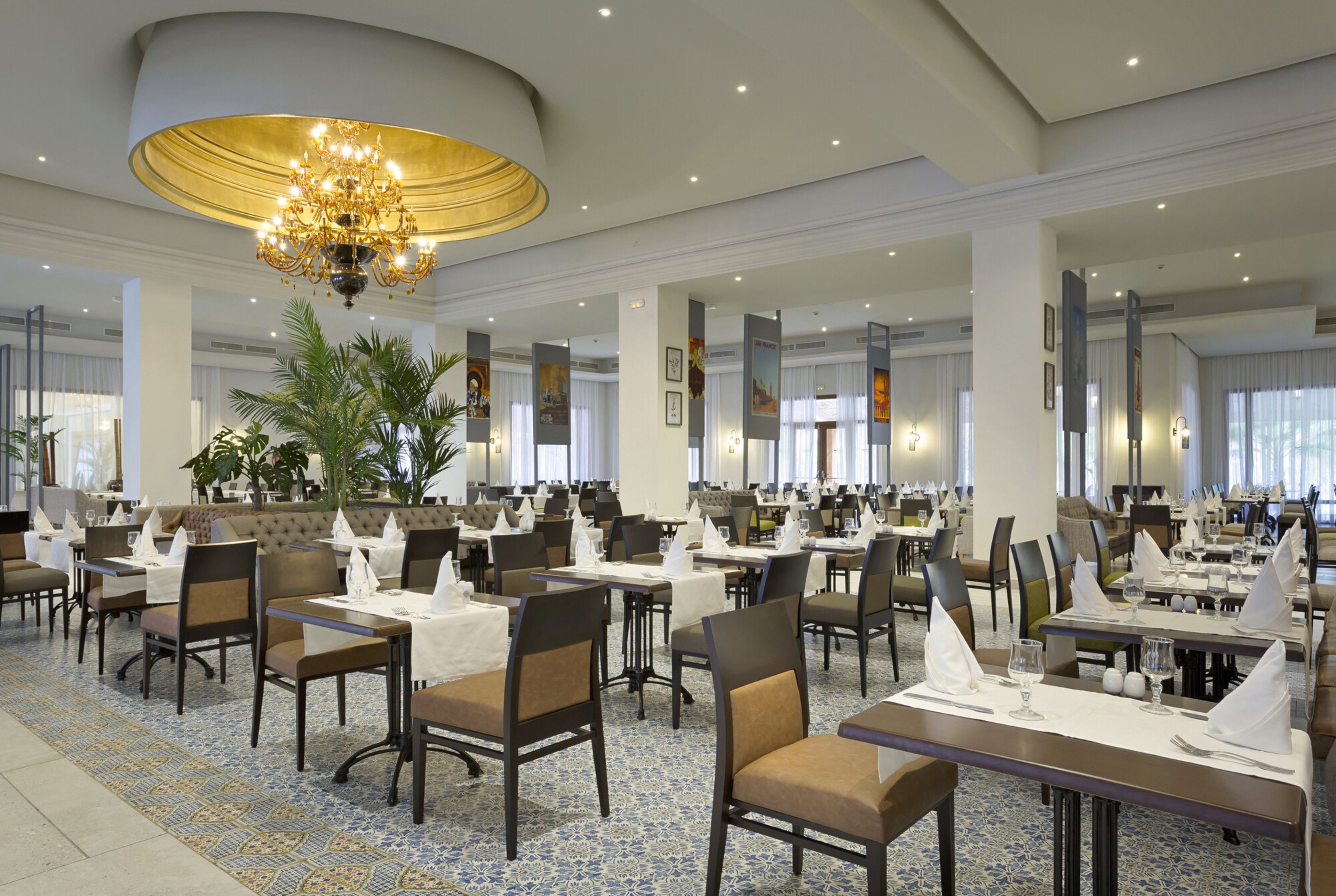 A spacious dining area with multiple tables and chairs, a large chandelier, and a patterned floor.
